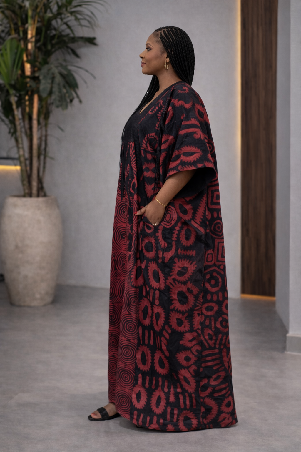 Woman wearing a red and black patterned dress standing indoors with a plant and door in the background.