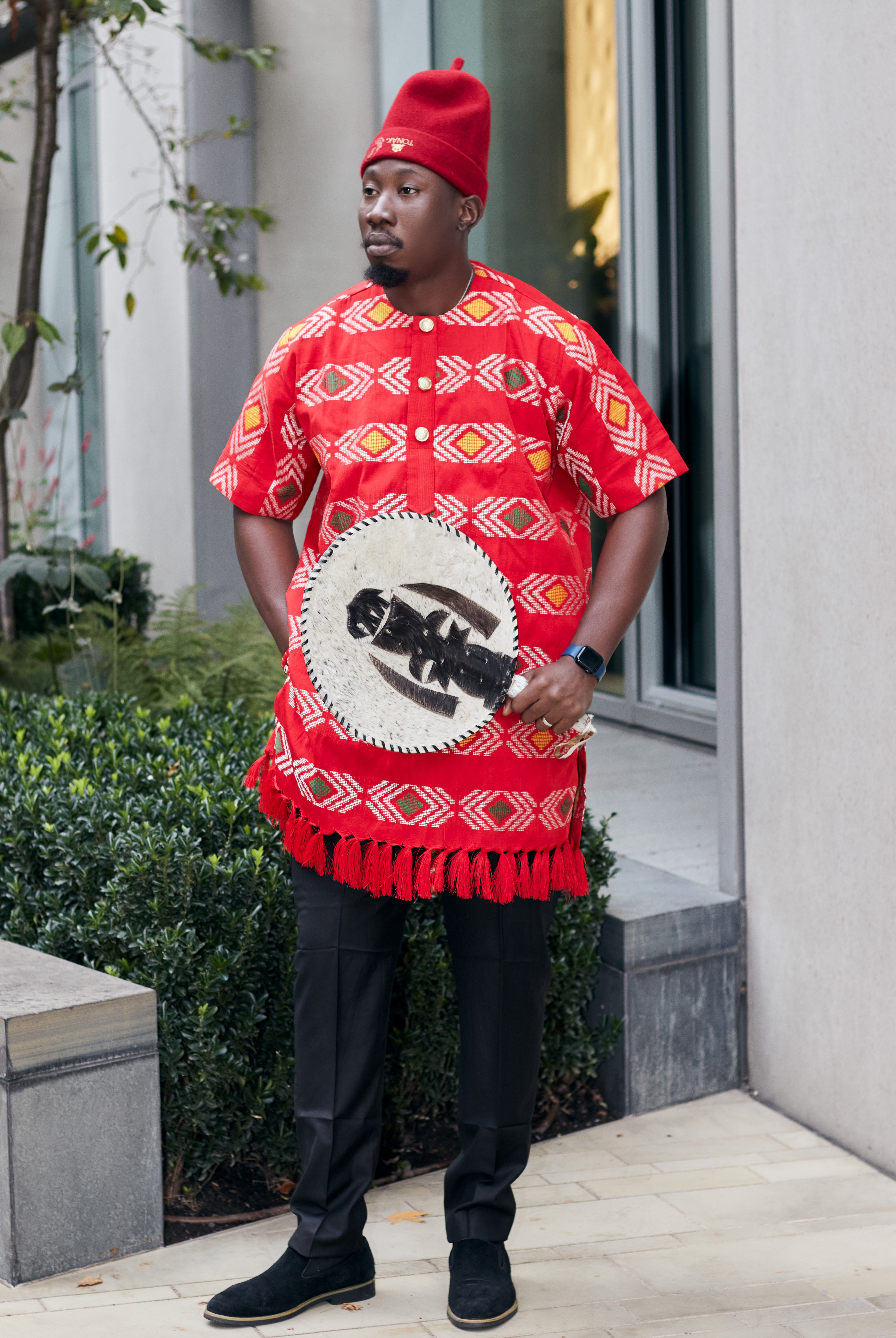 Person wearing a red traditional outfit with a white shield design, standing outdoors.