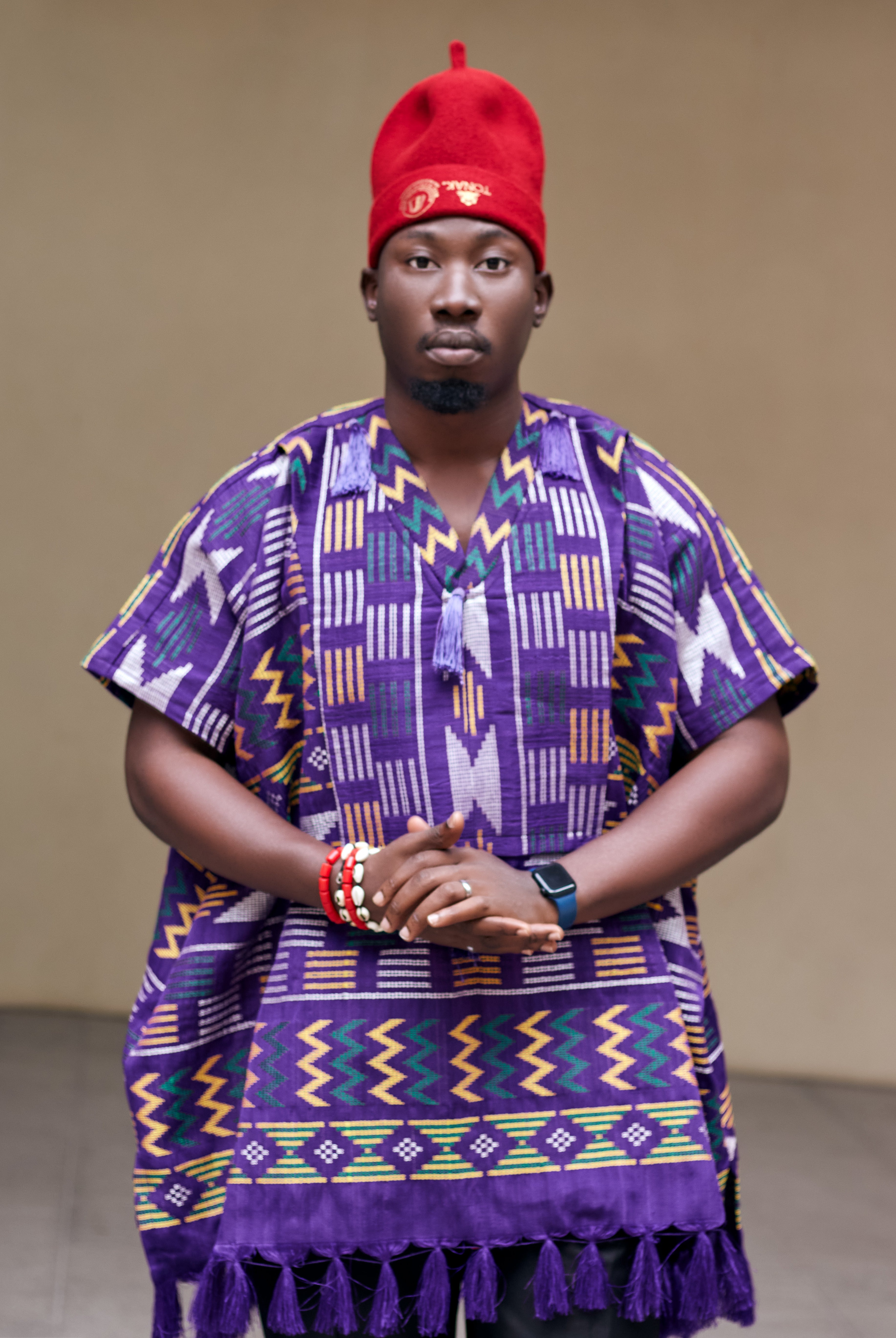 Person wearing a vibrant purple traditional outfit with a igbo traditional red cap
