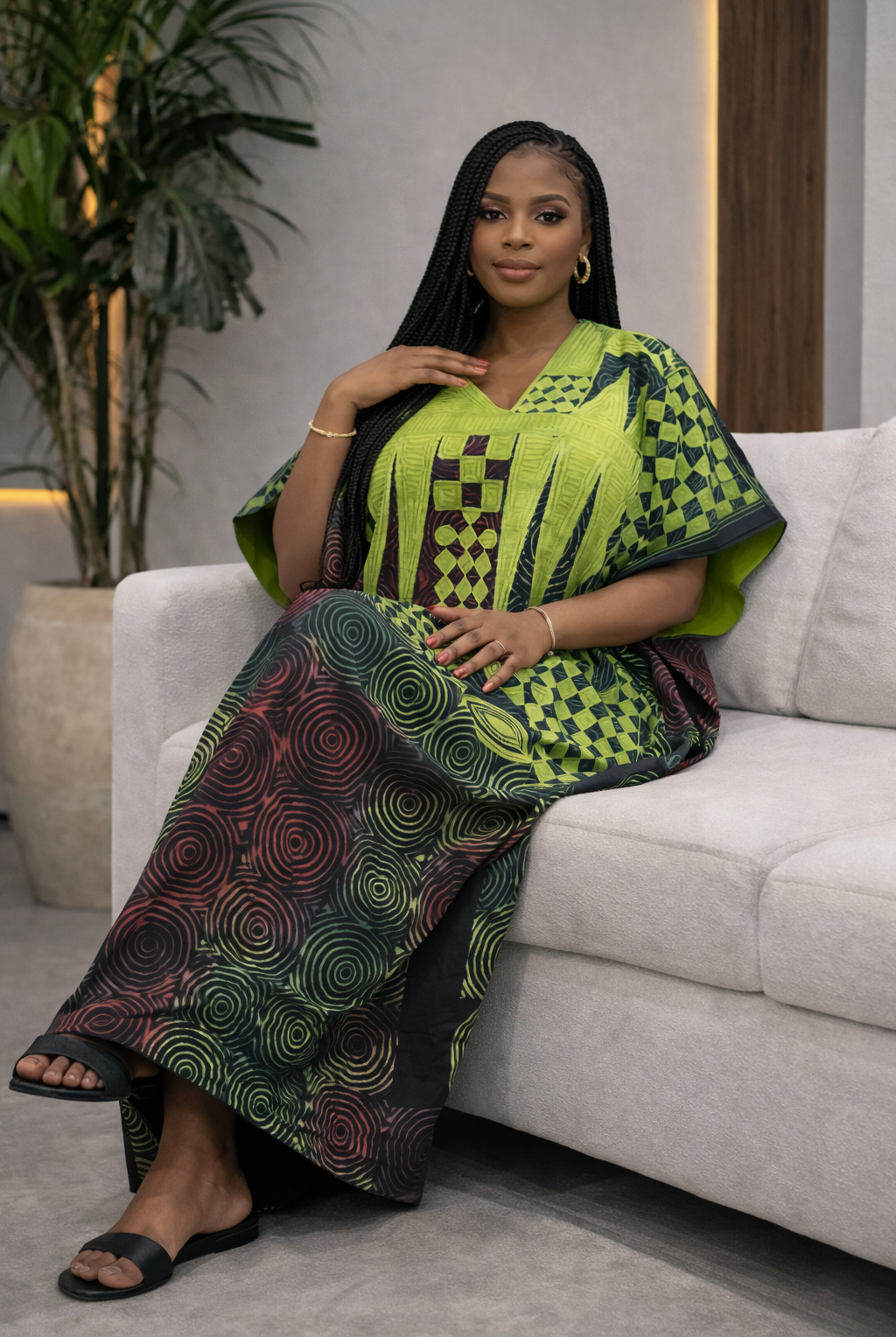 Woman in a green and black patterned outfit sitting on a couch.