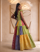 Woman wearing a colorful patchwork dress in an elegant indoor setting. African print maxi dress from CUMO London, trendy African clothing, summer outfits perfect for summer. Tiered maxi dress handmade with Adire