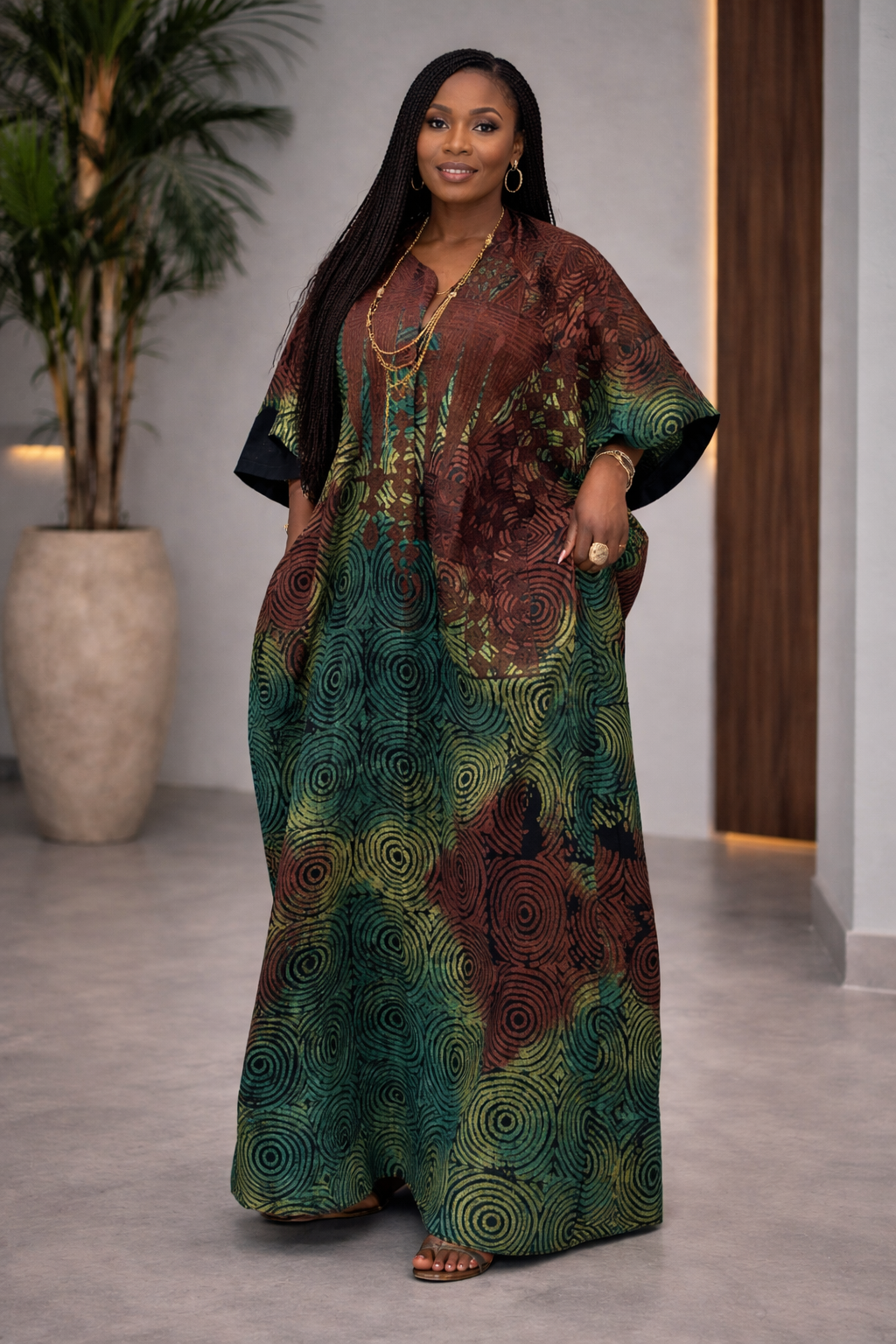 Woman wearing a patterned dress standing indoors with a plant and wooden door in the background.