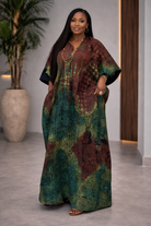 Woman wearing a patterned dress standing indoors with a plant and wooden door in the background.