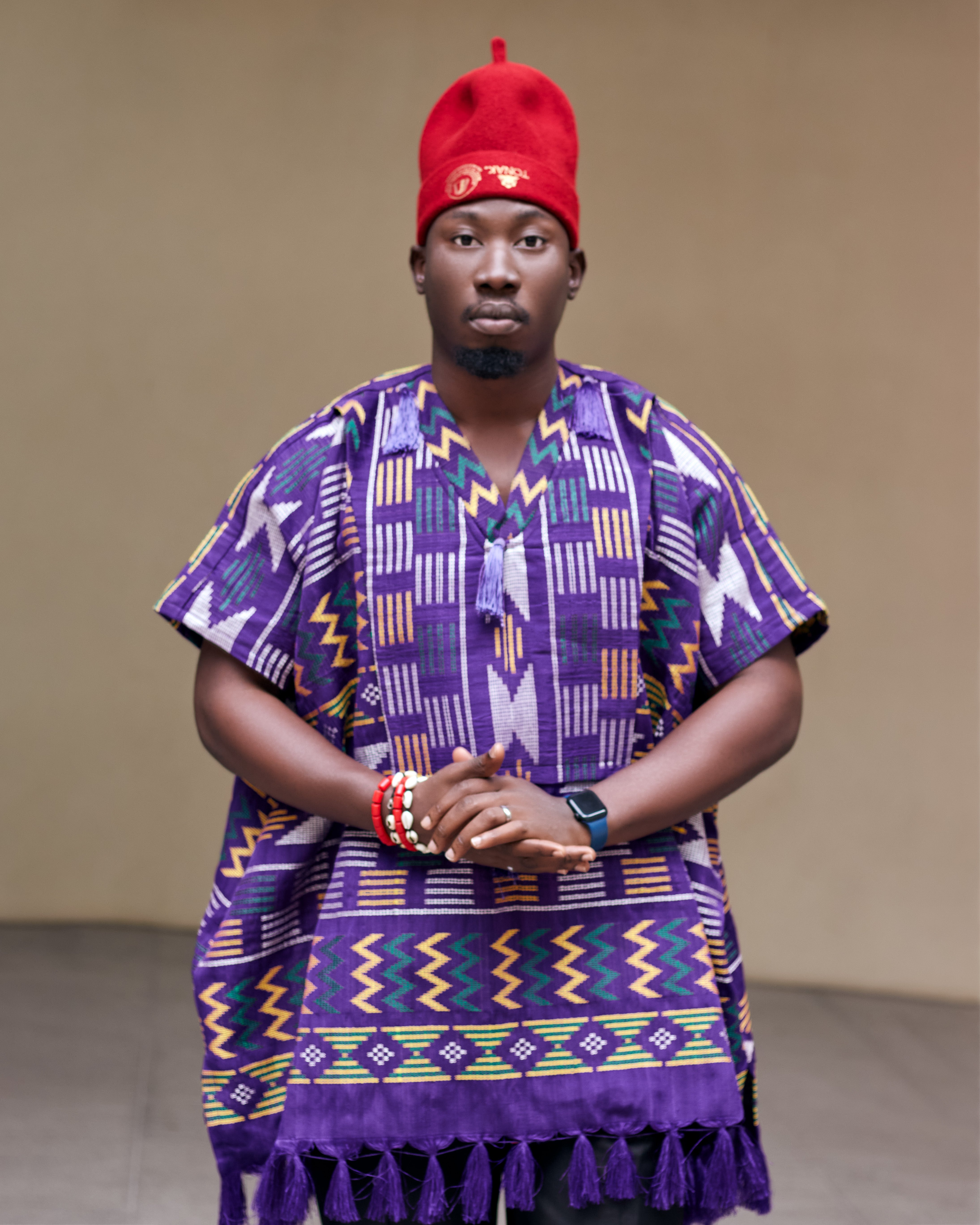 Person wearing a vibrant purple traditional outfit with a igbo traditional red cap 