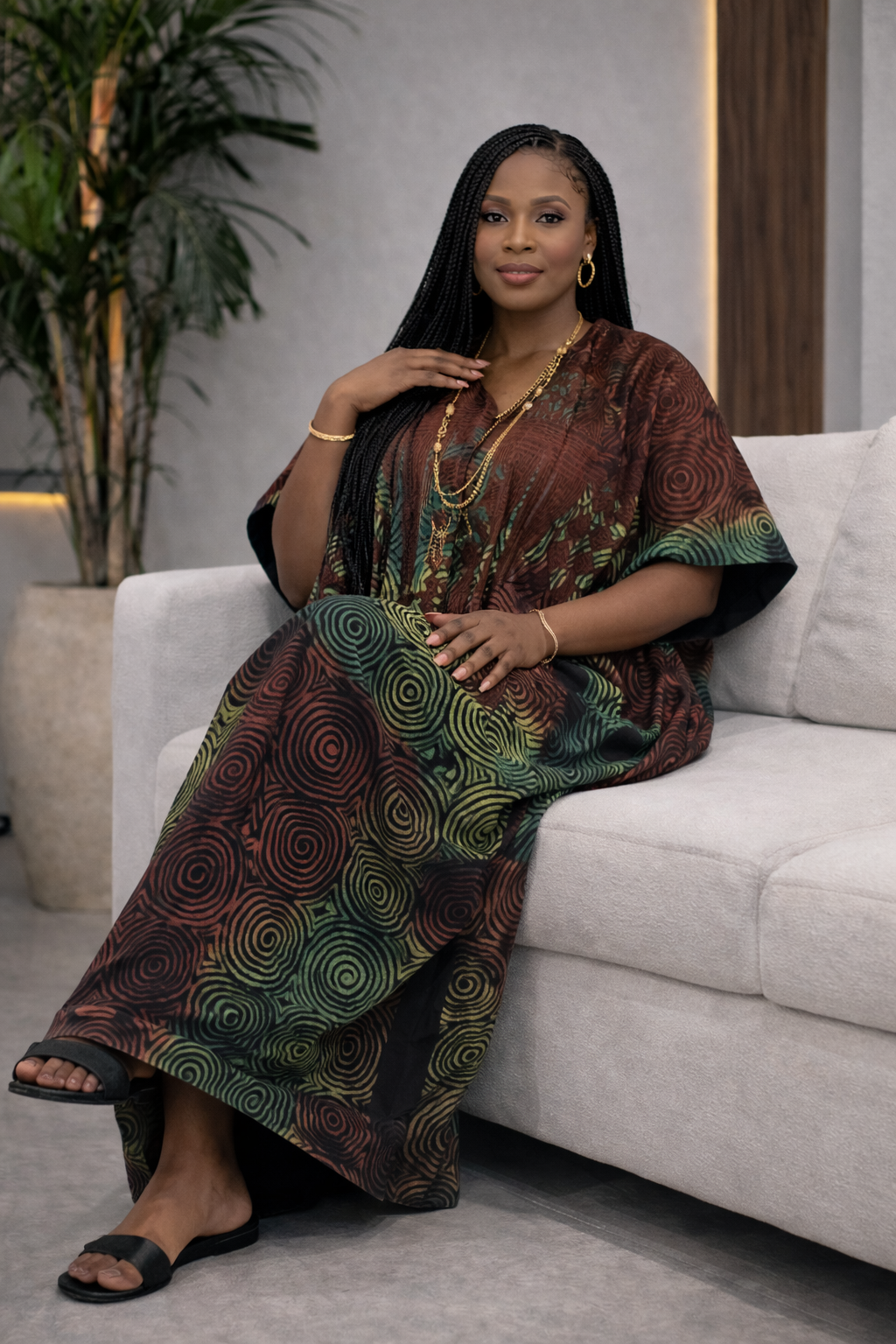 Woman in a patterned dress sitting on a couch with a plant in the background