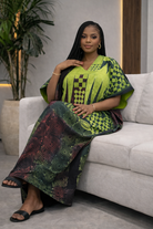 Woman in a green and black patterned outfit sitting on a couch.